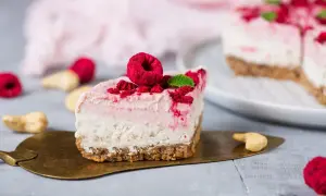 Ein Stück Himbeer Cheesecake mit frischen Himbeeren und Minze auf einem goldenen Tortenheber.