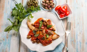 Un saporito pesce spada alla siciliana, condito con pomodorini, olive, capperi e menta fresca, pronto per essere gustato.