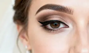 Oko kobiety z subtelnym makijażem ślubnym naturalnym. Brązowe cienie, kreska eyelinerem i podkreślone brwi.