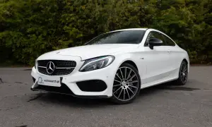 Biały Mercedes C43 AMG coupe z czarnymi felgami, zaparkowany na tle zieleni.