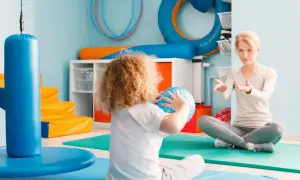 Dziecko z kędzierzawymi włosami bawi się piłką sensoryczną, a terapeuta wyjaśnia, integracja sensoryczna co to jest.