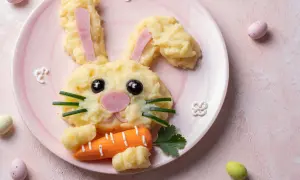 Un adorable lapin en purée de pommes de terre, parfait pour une entrée de Pâques sans œufs. Il tient une carotte et des œufs de Pâques sont autour.