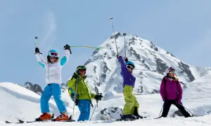 Famille en tenue de ski, bras levés, profitant du sport alpin sur une pente enneigée avec des montagnes majestueuses en arrière-plan.