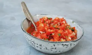 En skål med färsk pico de gallo, perfekt för ditt salsa recept. Tomater, lök och örter blandas i en rustik skål med en dekorativ sked.
