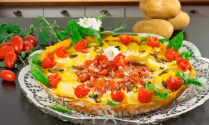 Herzhafte torta salata mit Kartoffeln, Tomaten und Kräutern, garniert mit frischem Basilikum und kleinen weißen Blüten.