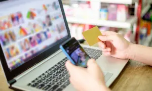 Dłoń trzymająca kartę płatniczą i telefon nad klawiaturą laptopa.