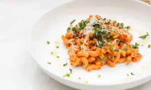Penne alla vodka z posiekaną natką pietruszki i startym parmezanem na białym talerzu.