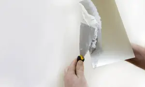 Dłoń trzyma szpachlę, nakładając masę sztablaturową na ścianę.