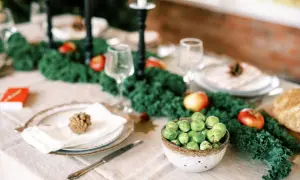 Vacker jul dukning med grönskande dekorationer, äpplen, kottar och en skål med brysselkål.
