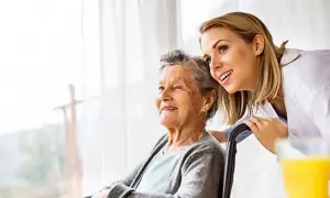 Uśmiechnięta opiekunka wspiera starszą panią na wózku. Troska i wsparcie w geriatrii.