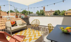 Un accogliente terrazzo sul tetto con divano, sedie colorate e un tappeto geometrico. Ideale per godersi il panorama urbano e rilassarsi.