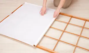 Mains déroulant du papier pour fabriquer une cloison japonaise sur un cadre en bois.