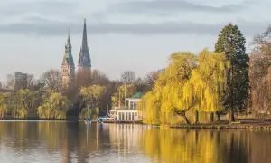 Ein idyllischer Blick auf den Alstersee in Hamburg. Sehens. Ein Bootshaus und die Türme der Stadt spiegeln sich im Wasser.