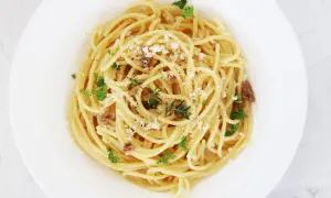 En tallrik med spaghetti, toppad med riven ost, färsk persilja och små bitar av sardeller. Enkel och smakrik pasta med sardeller.