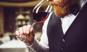 Uomo con barba rossa assapora un bicchiere di vino rosso durante una degustazione.