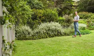 Mujer sonríe en un jardín exuberante, disfrutando del cuidado del césped en primavera. El césped verde y los arbustos floridos crean un paisaje idílico.