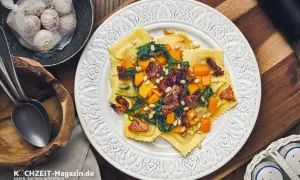 Ravioli mit Kürbis, Spinat und Pinienkernen – ein köstliches ravioli rezept. Daneben Knoblauch und Löffel.