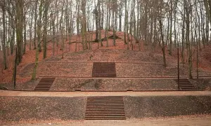 Wzgórze usypane z ziemi, pokryte opadłymi liśćmi, z kilkoma schodami prowadzącymi na szczyt. W tle las. To miejsce to Jaśkowa Dolina.