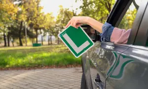 Mano sacando una L verde de autoescuela por la ventana de un coche. ¡Ya estoy lista para apuntarme a la autoescuela!