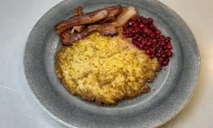 En gyllene raggmunk i ugn serveras med knaperstekt bacon och rårörda lingon på en grå tallrik.
