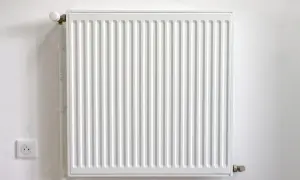 Biały kaloryfer żeberkowy na białej ścianie, z widocznym termostatem i gniazdkiem elektrycznym.