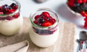 Zwei Gläser mit cremigem Dessert, gekrönt von Beeren und Fruchtsauce. Ein köstliches joghurtbombe rezept für den Sommer.