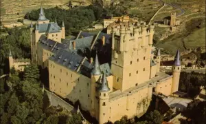 Vista aérea del Alcázar de Segovia, con sus torres y tejados, rodeado de vegetación. La sala de los reyes se intuye en su imponente estructura.