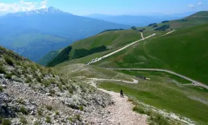Sentiero roccioso verso la Forca di Presta, con montagne verdi e un cielo azzurro.