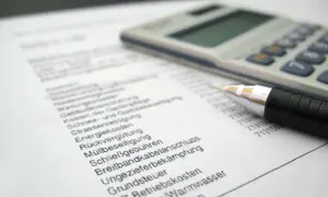 Rechnung mit Stift und Taschenrechner. Liste von Betriebskosten wie Heizung, Grundsteuer und Müllbeseitigung. Ein Widerspruch in der Betriebskostenabrechnung ist möglich.