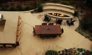 Un elegante giardino con un'area salotto attorno a un focolare, il tutto su un raffinato rivestimento in cemento per esterni.