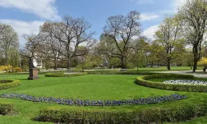 Piękny park miejski z rzeźbą, kwitnącymi rabatami i zielonymi trawnikami.