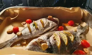 Dwie dorady ryby pieczone z cytryną, czosnkiem i pomidorkami koktajlowymi na papierze do pieczenia.