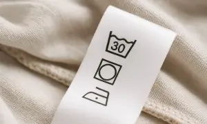 Metka z symbolami prania: pranie w 30°C, wybielanie dozwolone, prasowanie w niskiej temperaturze. Czy spodnie od garnituru można prać w pralce? Sprawdź metkę!