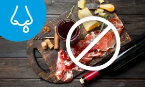 Na desce ser, wędliny i wino, przekreślone symbolem zakazu. Obok symbol nosa z kropelką, sugerujący dietę antyhistaminową.