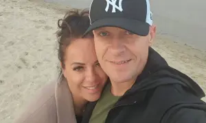 Piotr Marciniak z żoną na plaży, uśmiechnięci i blisko siebie.
