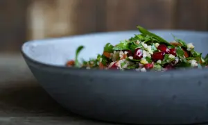 Frischer Tabouleh-Salat mit Granatapfelkernen und Petersilie in einer grauen Schüssel. Ein köstliches Rezept für den Sommer.
