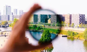 Dłoń trzyma okrągły filtr, przez który widać miasto z pociągiem. Efekt filtrów w fotografii.