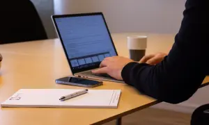 Person arbetar vid laptop, med mobil och anteckningsblock på bordet. Kanske planerar att låna ut pengar till aktiebolag.