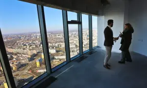 Para dyskutuje o cenach mieszkań, patrząc na panoramę miasta z okna wieżowca.