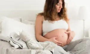Kobieta w ciąży, z rękami na brzuchu, obok koszyka z ubrankami i zabawką. Obraz symbolizuje nadzieję i oczekiwanie, ale może też nawiązywać do trudnych doświadczeń, jak martwe dziecko w brzuchu objawy.