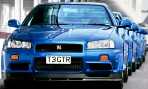 Błękitny Nissan Skyline GT-R R34 z tablicą "T3 GTR" ustawiony w rzędzie z innymi.
