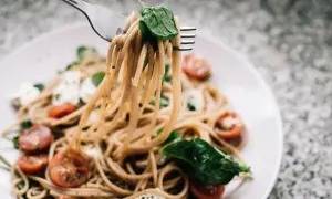Widok z bliska na makaron z pesto ze słoika i śmietaną, z pomidorkami koktajlowymi i mozzarellą.