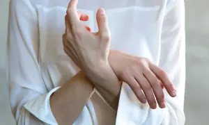 Frau hält ihr Handgelenk, als ob sie einen stechenden Schmerz im Handgelenk bei Drehbewegung spürt.