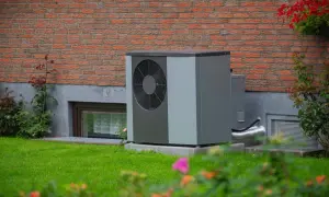 Solidny fundament pod pompę ciepła zapewnia stabilność urządzenia. Urządzenie stoi na trawniku przy ceglanym domu.