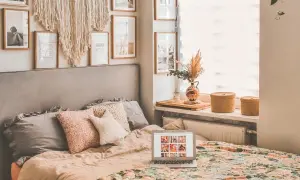 Przytulna sypialnia w stylu boho z łóżkiem, makramą na ścianie i laptopem.