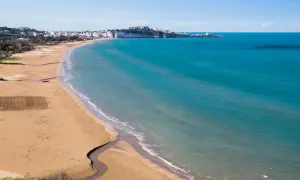 La spiaggia della Scialara si estende con sabbia dorata e mare azzurro, con il borgo bianco arroccato sulla scogliera in lontananza.