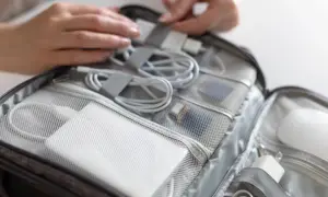 W torbie podróżnej schludnie ułożone kable, ładowarki i powerbank do samolotu. Dłonie porządkują akcesoria.