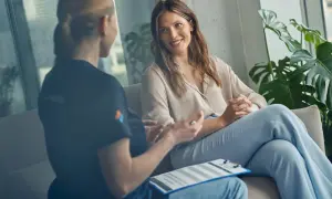 Dwie kobiety rozmawiają w jasnym pomieszczeniu, jedna z nich uśmiecha się.