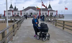 Kobieta z wózkiem na molo w Ahlbecku. W tle historyczny budynek i plaża, idealne miejsce na rodzinne atrakcje.