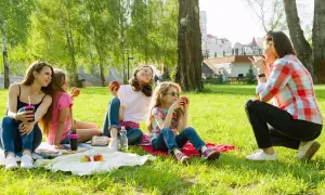 Rodzina na pikniku w parku. Czy Boże Ciało jest dniem wolnym od pracy? Dzieci jedzą jabłka, ciesząc się słońcem.